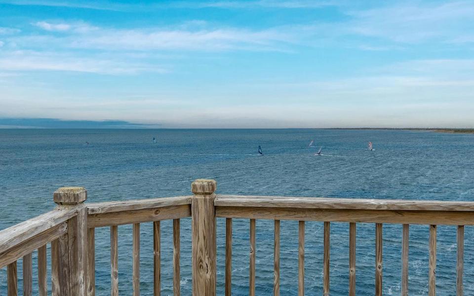 View of the Pamilico sound over the handrail of a vacation home reveals windsurfers dotting the water in the distance